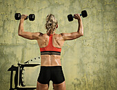 Rear view of athlete woman exercising with dumbbells