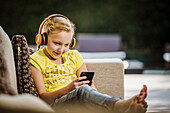 Smiling girl (10-11) with headphones and smart phone sitting on sofa