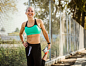 Athlete woman in sports clothing stretching at fence