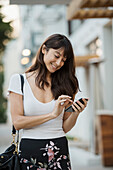 Lächelnde Frau, die in der Stadt auf ihr Smartphone schaut
