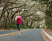 Frau joggt auf einer mit Bäumen gesäumten Landstraße