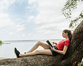 Frau sitzt auf einem Baum und liest ein Buch