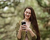 Lächelnde Frau schaut auf ihr Smartphone im Park