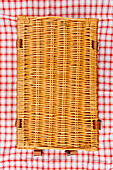 Overhead view of closed wicker picnic basket on plaid tablecloth