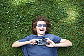 Im Gras liegender Junge mit Kamera