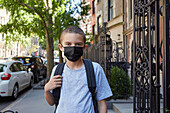 USA, New York, New York City, Portrait of boy (8-9) in face mask standing on sidewalk