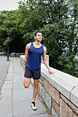 USA, New York, New York City, Mann in Sportkleidung streckt sich an einer Mauer im Park