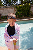 Lächelnder Junge (8-9), eingewickelt in ein Handtuch, steht am Pool