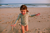 Lächelndes Mädchen (2-3) spielt am Strand bei Sonnenuntergang