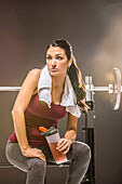 Studio shot of woman in sleeveless top sitting at barbell