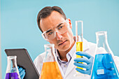 Scientist with digital tablet looking at yellow liquid in beaker