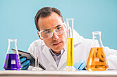 Scientist with digital tablet looking at yellow liquid in measuring beaker