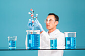 Scientist holding molecule model, blue liquid in beakers in foreground