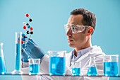 Scientist holding molecule model, blue liquid in beakers in foreground