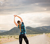 Vereinigte Staaten, Utah, Cedar Fort, Rückansicht einer Frau beim Stretching auf der Straße in der Wüstenlandschaft