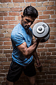 Man exercising with dumbbell against brick wall