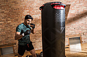 Mann trainiert mit Boxsack im Fitnessstudio