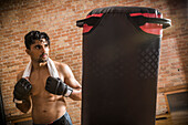Mann ohne Hemd, mit Boxhandschuhen und Handtuch im Fitnessstudio