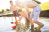 Jungen ohne Hemd (8-9) schwimmen mit einem Papierboot auf einem Fluss