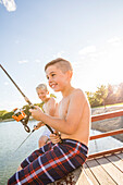 Smiling shirtless boys (8-9) fishing on lake
