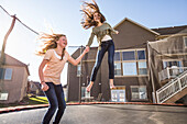 Girls (10-11, 12-13) jumping on trampoline in front of house