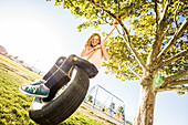 Smiling girl (10-11) on tire swing in garden