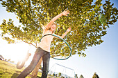 Girl (12-13) spinning hula hoop, sister (10-11) on tire swing in background