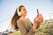 Smiling girl (12-13) with headphones and smart phone in park