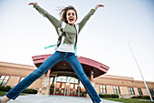United States, Utah, Lehi, Smiling girl (12-13) jumping in front of school building