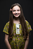 Studio-Porträt eines lächelnden Mädchens (10-11) in grünem Kleid mit Blume im Haar