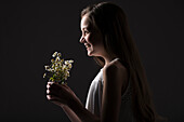 Profil eines lächelnden Mädchens (10-11) mit einem Strauß Wildblumen vor schwarzem Hintergrund