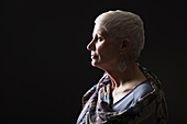 Profile of woman with white short hair wrapped in shawl against black background
