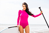 Frau in rosa Badeanzug hält Paddelbrett und Ruder 