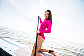 Woman in pink swimsuit kneeling on paddleboard on lake