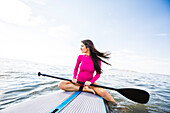 Woman in pink swimsuit sitting on paddleboard on lake