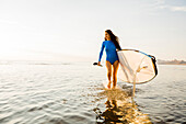 Frau im blauen Badeanzug mit Paddleboard im See bei Sonnenuntergang