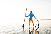 Portrait of woman in blue swimsuit with paddleboard in lake at sunset
