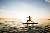Woman doing yoga on paddleboard at sunset 