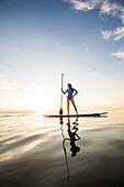 Frau steht bei Sonnenuntergang auf einem Paddleboard 