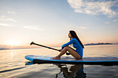Frau auf Paddleboard sitzend bei Sonnenuntergang 