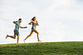 Frau und Mann rennen auf einem Grashügel im Park 