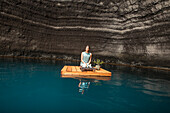 Beautiful woman kneeling on wooden raft on pond