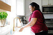 Frau wäscht sich die Hände am Spülbecken in der Küche