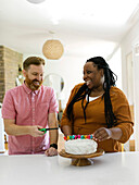 Lächelndes Paar zündet Geburtstagskerzen auf Kuchen an