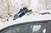 USA, New Mexico, Santa Fe, Frau mit Gesichtsmaske räumt Schnee aus dem Auto