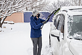 USA, New Mexico, Santa Fe, Frau mit Gesichtsmaske räumt Schnee aus dem Auto