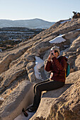 USA, New Mexico, Los Alamos, Tsankwai, Wanderin fotografiert mit Smartphone auf Felsen sitzend im Bandelier National Monument