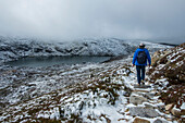 Australia, New South Wales, Woman hiking on snowy trail by lake at Charlotte Pass in Kosciuszko National Park