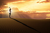 Dubai, Vereinigte Arabische Emirate, Frau übt Yoga auf einer Sanddüne in der Wüste bei Sonnenuntergang