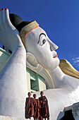 Myanmar, Monyma, Mandalay Division, Novice monks standing under giant statue of reclining Buddha in Lay Kyune Sakkyar temple